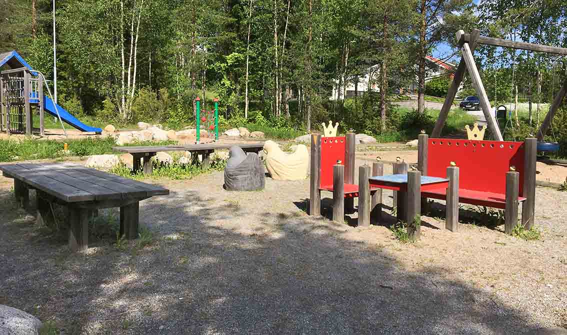 Bankar målade i rött med kungakronor på överkanten. Två små kycklingar att rida på i bakgrunden samt bänkar och klättertorn med rutschkana