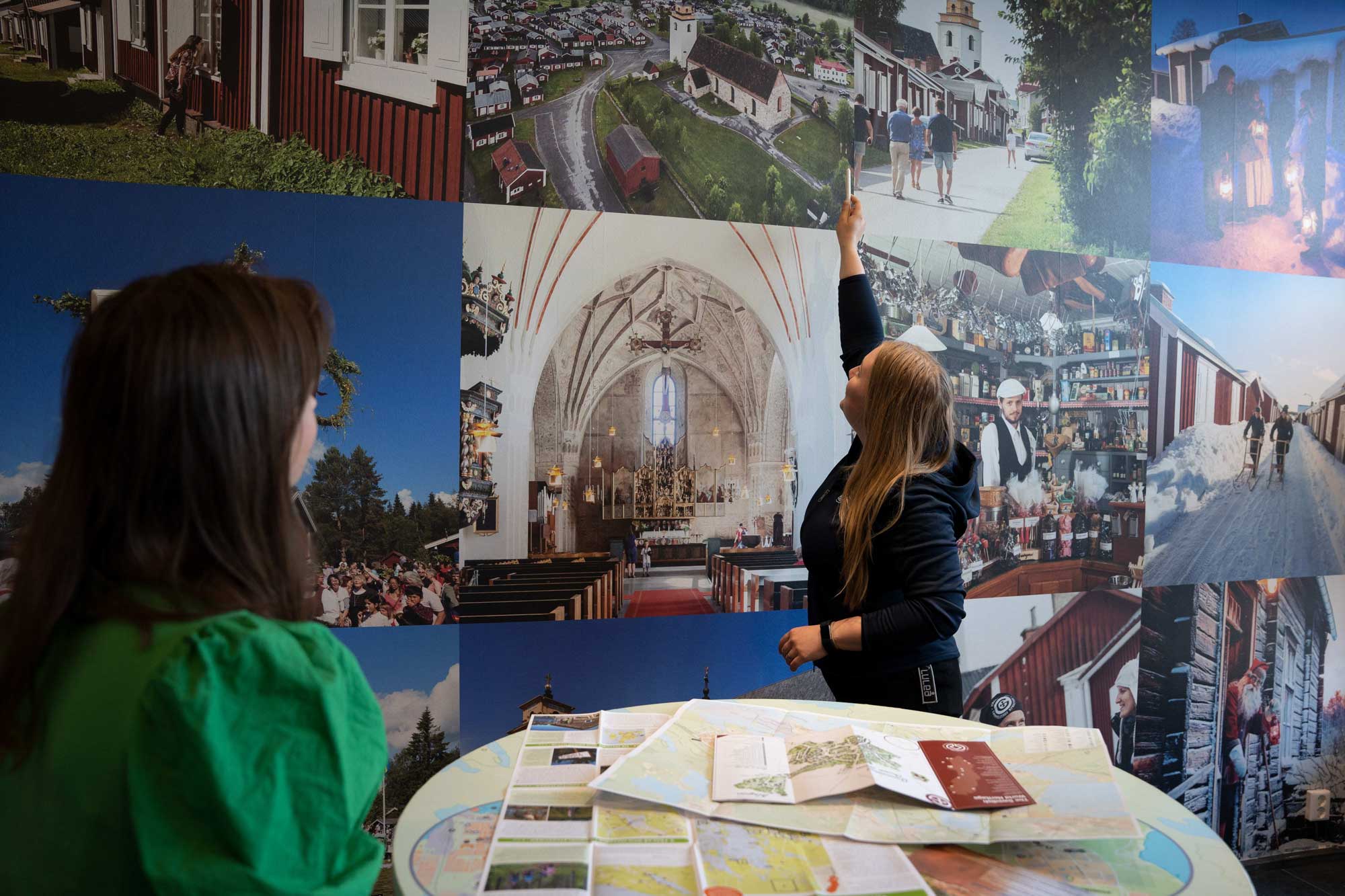 En turistinformatör pekar på en vägg med bilder av Gammelstads kyrkstad.