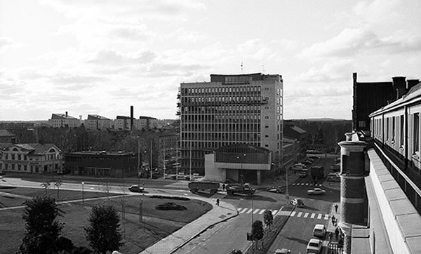 Vy över stadsgata och park med högt hus i bakgrunden.