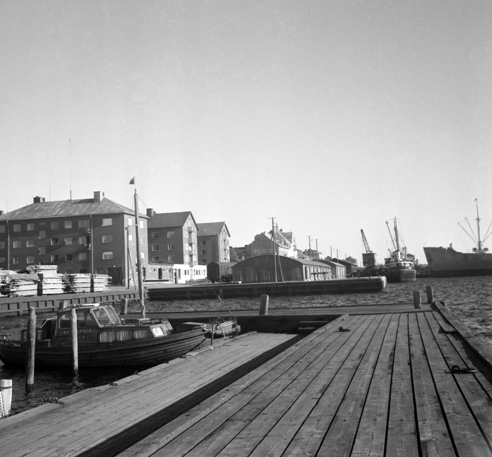 Vy över hamn med brygga. I bakgrunden flerbostadshus.